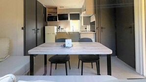 Un espacio habitable compacto con kitchenette, una zona de comedor con dos sillas y un pequeño rincón de descanso.