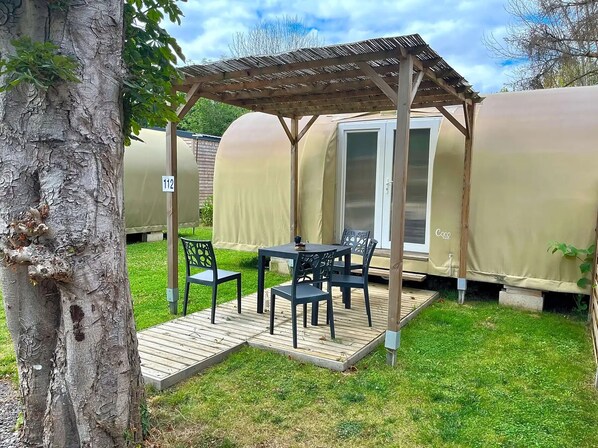 Un área de estar al aire libre techada con una mesa, sillas, una pérgola y una estructura similar a una tienda con una puerta corrediza.
