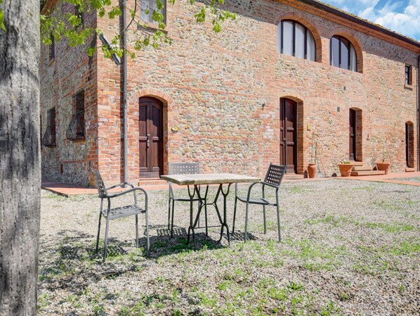 A stone building with arched windows and doors, a gravel courtyard, and outdoor furniture.