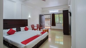 A hotel room with a large bed, a ceiling fan, a balcony with a view, and a door leading to the outside. - Periyar Holidays  (Peermade)