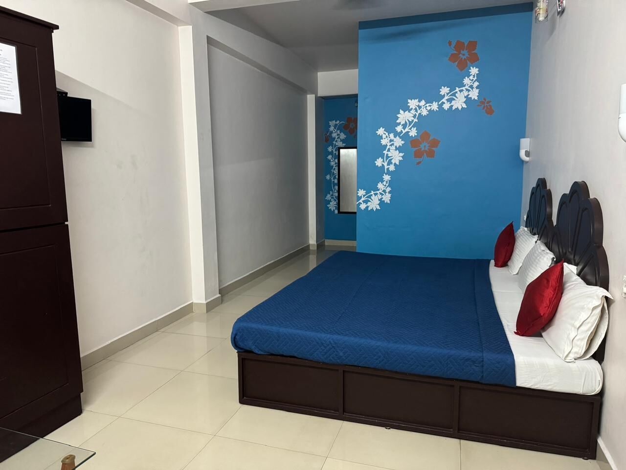Quarto com cama, almofadas e parede azul decorada com desenhos florais.