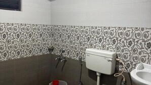 A small bathroom with a toilet, sink, and shower. The walls have patterned tiles, and the floor is tiled. - Periyar Holidays  (Peermade)