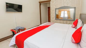 A neatly made bed with a red and white bedspread, a television mounted on the wall, and a mirror above the bed.