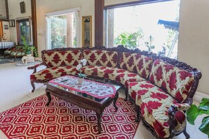 Un salón con un sofá estampado, una mesa de centro de vidrio y una alfombra con diseño rojo y blanco.