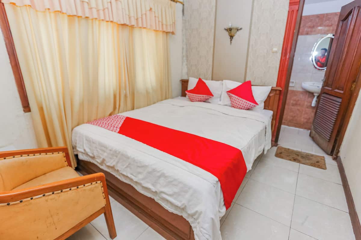 Ein Schlafzimmer mit Bett, einem Sessel und einem durchgegangenen Tür sichtbaren Badezimmer.