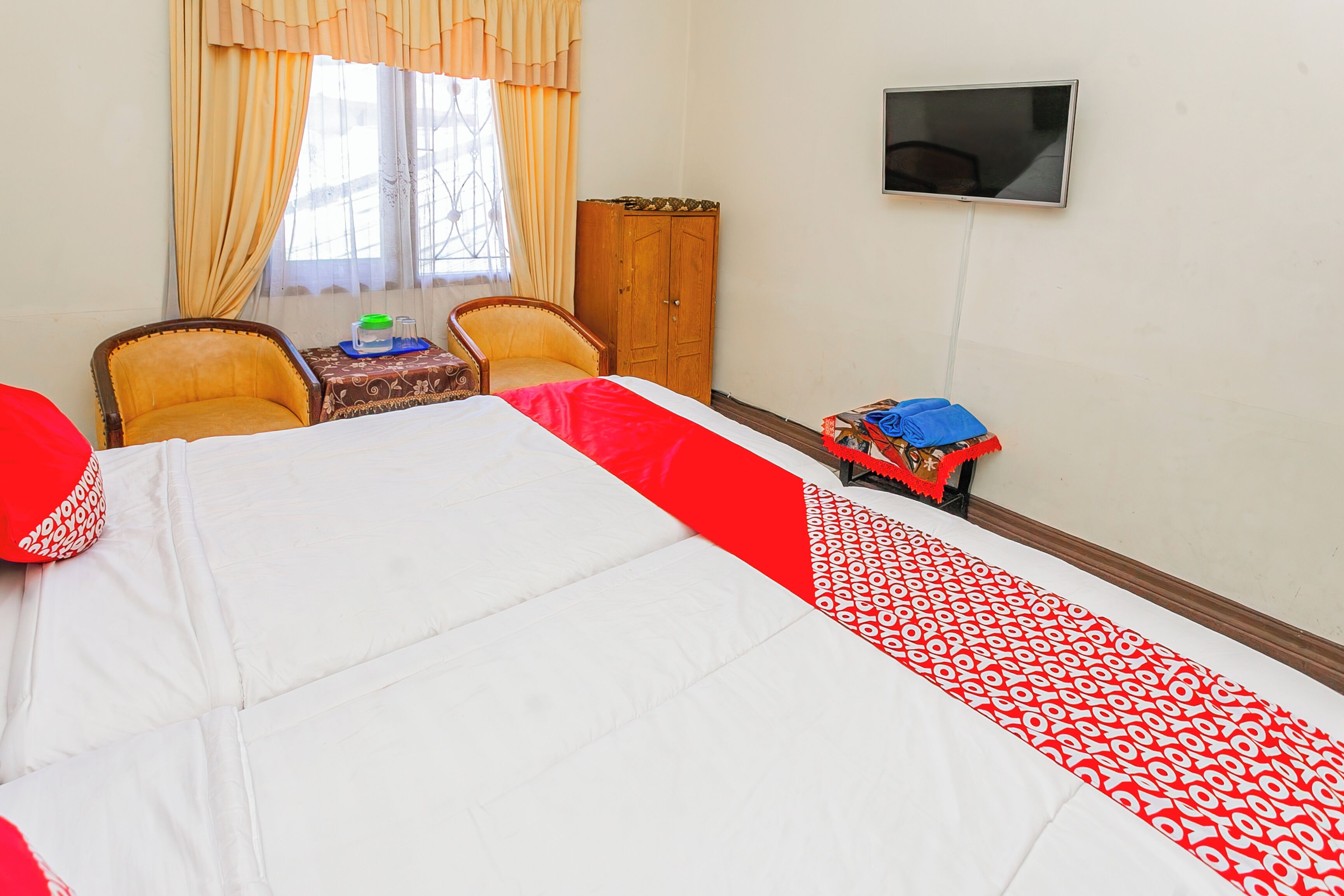 Een hotelkamer met een bed, twee stoelen, een tafeltje, een kast en een televisie.