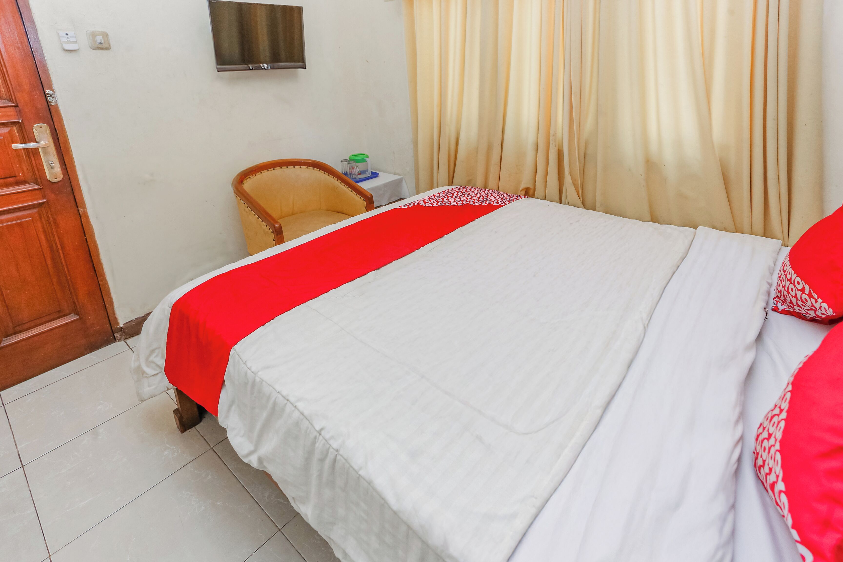A hotel room with a bed, a chair, a small table, and a TV on the wall.