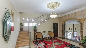 A staircase with a red floral carpet, two chairs, a small table, and a chandelier. - Collection O Puncak Bogor Near Taman Safari Indonesia Formerly Hotel Andalus (Megamendung)