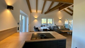 A modern kitchen with a central island, wooden beams, and a dining area with a sofa and table. - Attic Apartment in Saalfelden Near Ski Slopes (Saalfelden am Steinernen Meer)