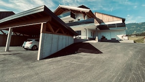 A modern two-story house with a covered driveway and a car parked inside. - Attic Apartment in Saalfelden Near Ski Slopes (Saalfelden am Steinernen Meer)