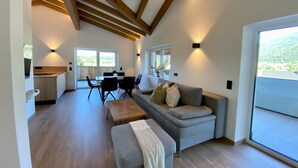 A spacious living area with a sofa, ottoman, and dining table. There is a kitchen area with a window and a view of the outdoors. - Attic Apartment in Saalfelden Near Ski Slopes (Saalfelden am Steinernen Meer)