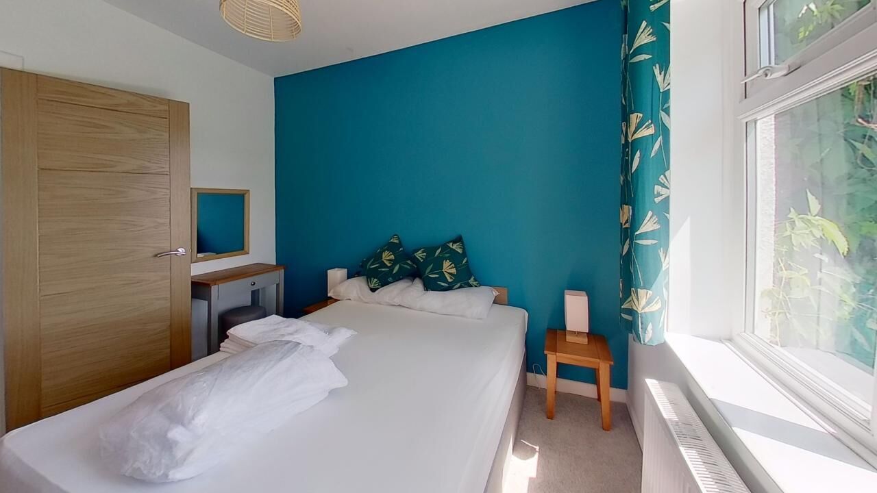 Une chambre à coucher comprenant un lit, une armoire en bois, une table de chevet, une commode, un miroir et une fenêtre avec des rideaux.
