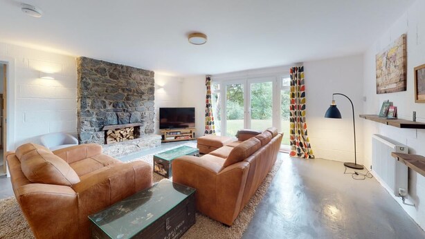 Una sala de estar moderna con chimenea de piedra, sofás de cuero, un televisor de pantalla plana y un gran ventanal con cortinas coloridas.