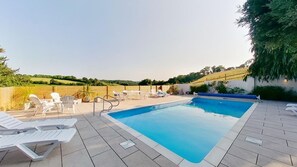 A rectangular swimming pool with a tiled deck, surrounded by white lounge chairs and a wooden fence. - Rural house, private heated pool and plenty of space (Littlehempston)