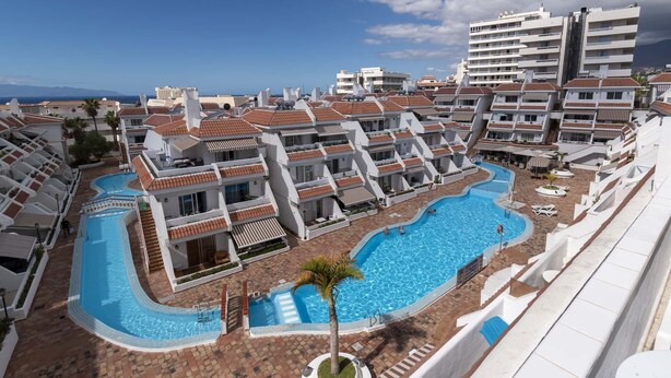 Un complexe hôtelier comprenant plusieurs bâtiments, une piscine centrale et offrant une vue sur la mer.