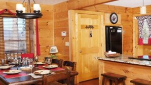 A wooden interior with a dining table set for four, a kitchen area with a refrigerator, and a wooden ceiling with a decorative design. - Escape to Serenity: Cozy Mountain Cabin with Mountain View/Pet Friendly (Sevierville)