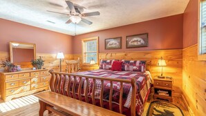 A cozy bedroom with a wooden headboard, a wooden dresser, a bench, and a ceiling fan. - Escape to Serenity: Cozy Mountain Cabin with Mountain View/Pet Friendly (Sevierville)