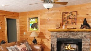 A cozy living room with a leather sofa, a fireplace, a ceiling fan, and a patterned rug. - Escape to Serenity: Cozy Mountain Cabin with Mountain View/Pet Friendly (Sevierville)