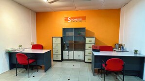 Egy szoba, amelyben két íróasztal, piros székek, egy mennyezeti ventilátor és egy „Homestay Premium” felirattal ellátott tábla található.