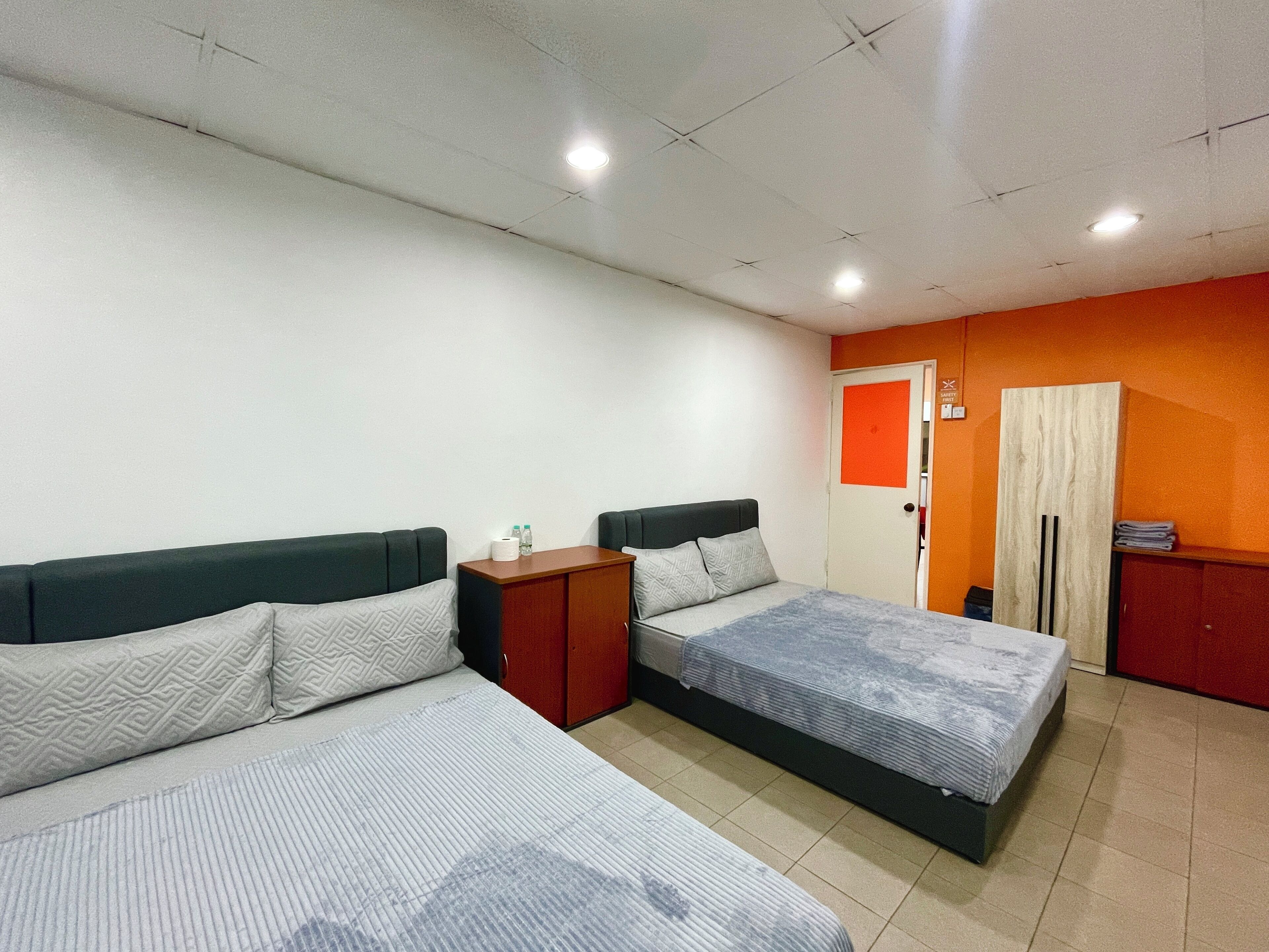 Habitación con dos camas, una mesita de noche de madera, un armario y una puerta con un panel naranja.