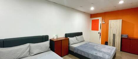 Habitación con dos camas, una mesita de noche de madera, un armario y una puerta con un panel naranja.