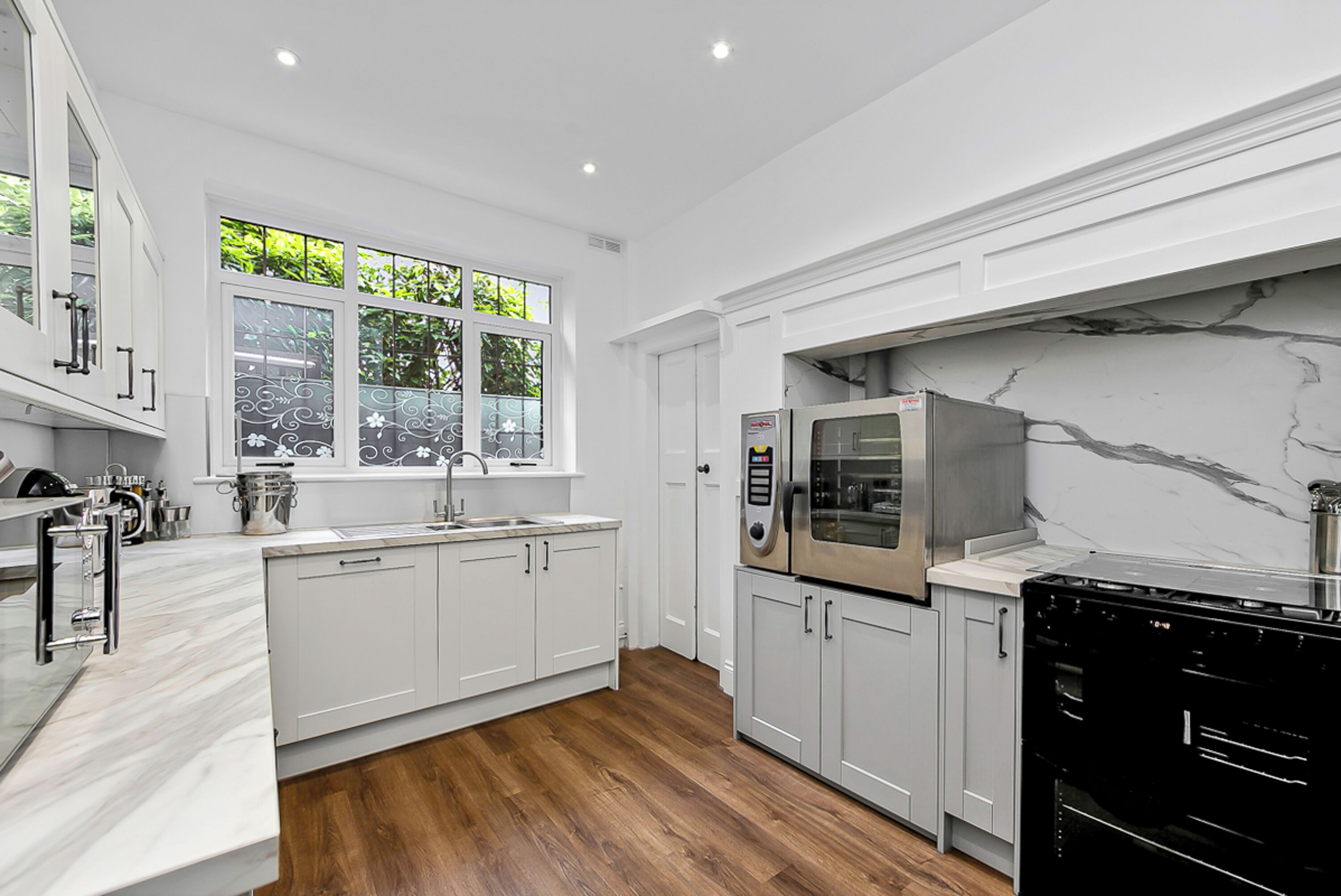 A modern kitchen with white cabinetry, a marble backsplash, and stainless steel appliances.