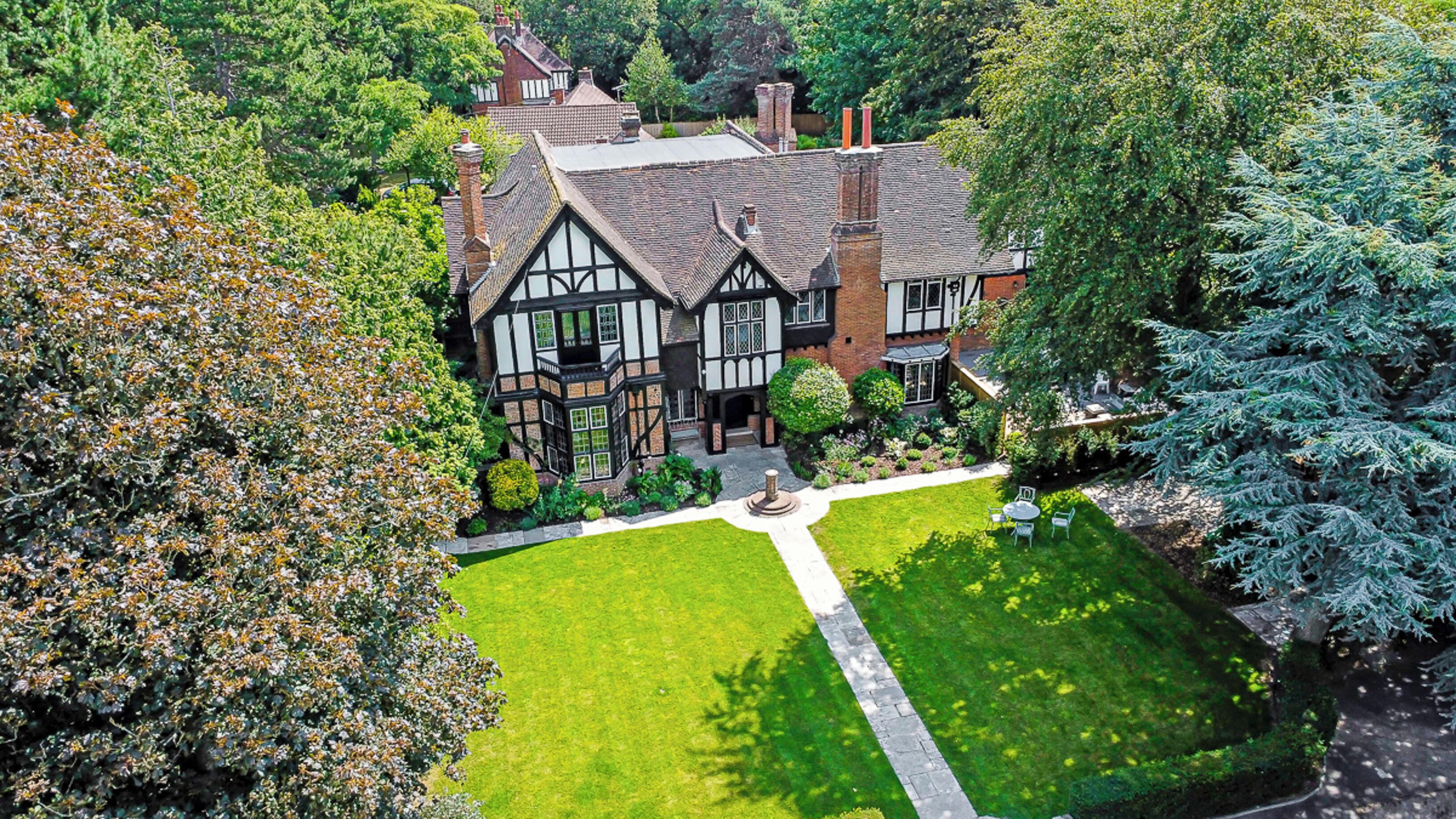 A Tudor-style house with a well-maintained lawn and a central garden feature.