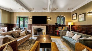 A spacious living room with a fireplace, comfortable seating, a flat-screen TV, and a bookshelf. - Mansion by the Sea, 12BR/12BA, Perfect for Events (Bournemouth)