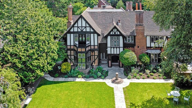 A Tudor-style house with a symmetrical facade, multiple chimneys, and a well-maintained garden with a lawn and a fountain. - Mansion by the Sea, 12BR/12BA, Perfect for Events (Bournemouth)