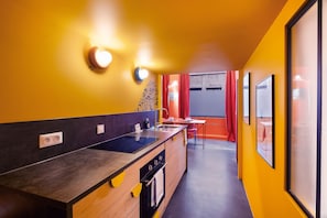 Eine moderne Küche mit schwarzem Arbeitsplatz, Holzschränken und einem eingebauten Backofen. Im Hintergrund befindet sich ein Fenster mit roten Vorhängen und ein Tisch mit Stühlen.