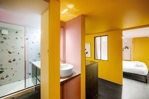 Ein modernes Badezimmer mit Glasdusche, Waschbecken in Weiß und einem Bett mit weißer Bettwäsche.