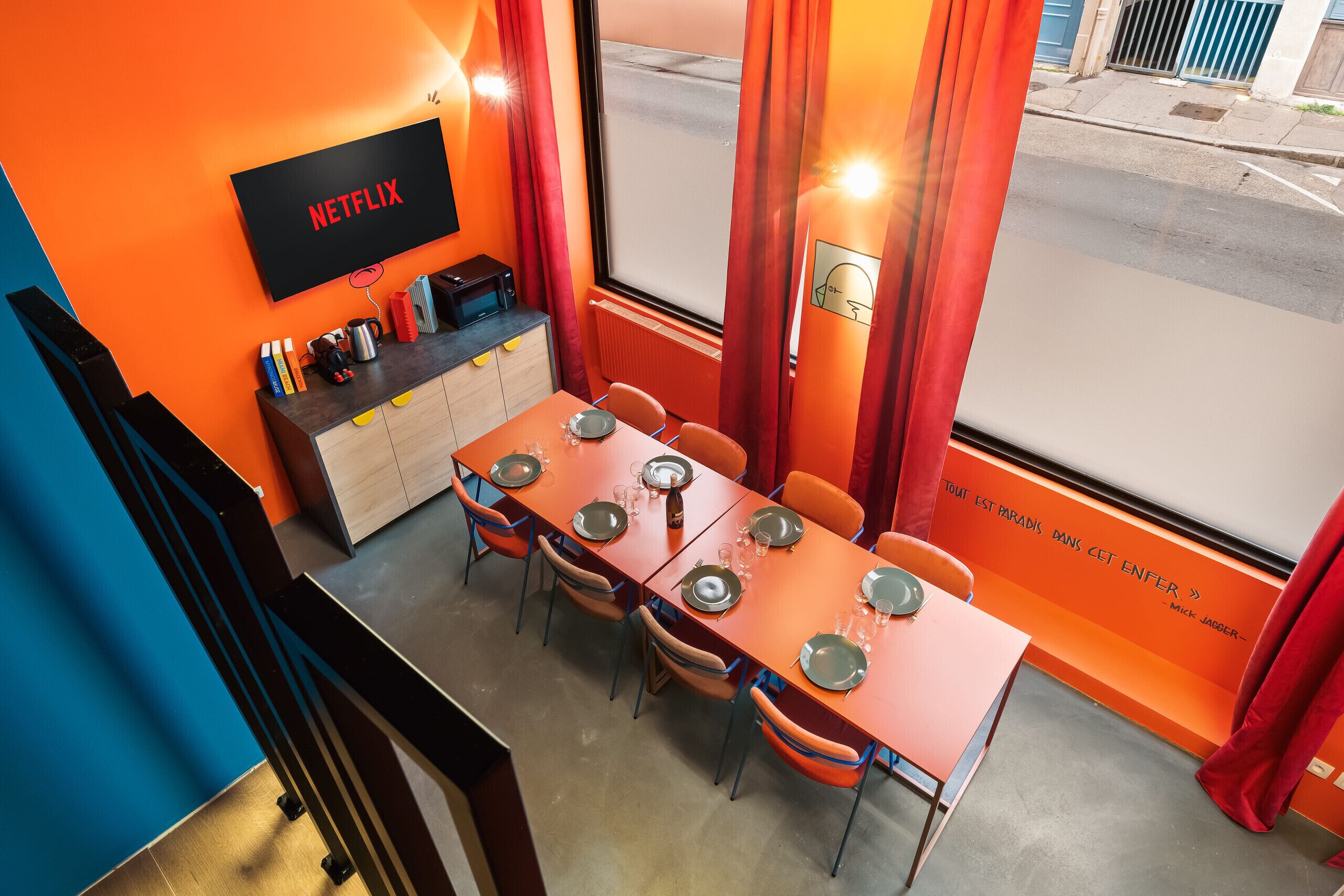 Un comedor con una mesa preparada para cuatro, una pantalla de televisión mostrando 'NETFLIX' y vista a la calle.