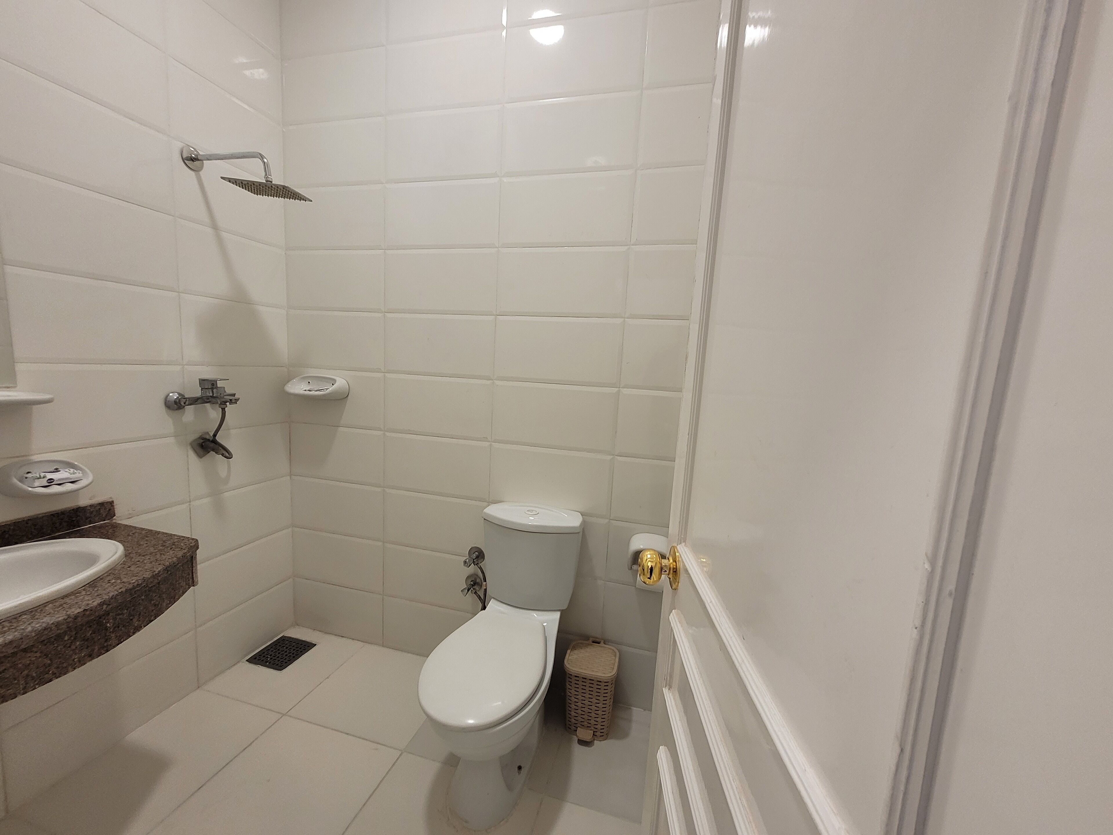 Ein Badezimmer mit weißen Fliesen, einer Toilette, einer Dusche und einem Waschbecken.