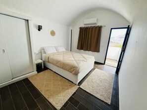 Un dormitorio con cama, mesita de noche, aire acondicionado instalado en la pared y vista a través de una puerta.