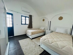 A bedroom with two beds, a window with curtains, a nightstand, and a wall-mounted air conditioner.