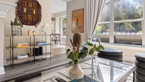 A living room with a glass coffee table, a bookshelf, a decorative rug, and a window with a view of trees. - Eclipse · Artist Retreat @ Cypress Creek | Hotub | Sleeps 9 (Cedar Park)