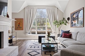 A living room with a fireplace, a sofa, a coffee table, and a large window with curtains.