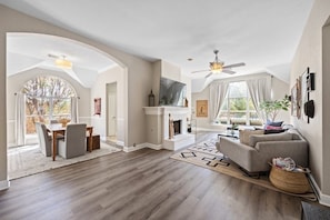 A spacious living room with a fireplace, a dining area, and a large window.