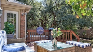 A patio with wicker furniture, a glass table, and a sign with a logo. - Eclipse · Artist Retreat @ Cypress Creek | Hotub | Sleeps 9 (Cedar Park)