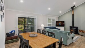 Un salon chaleureux avec une table à manger en bois, un canapé bleu et un téléviseur. Il y a une cheminée et une fenêtre avec des stores.