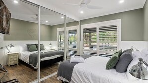 Une chambre dotée d’un grand miroir, de deux lits, d’un ventilateur de plafond et offrant une vue sur l’extérieur par la fenêtre.