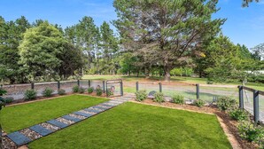 Un jardin bien entretenu, doté d’un chemin pavé, d’une zone délimitée par une clôture et d’une variété d’arbres.