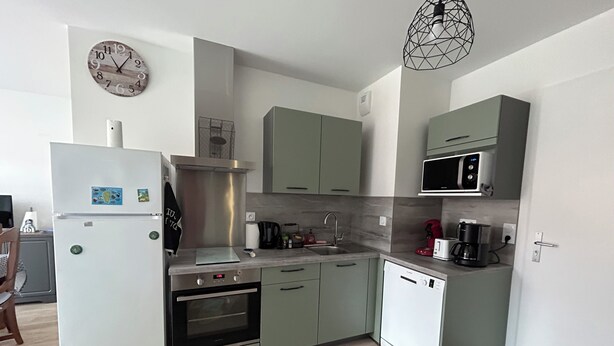Una cocina moderna con horno empotrado, microondas y lavavajillas. Hay un lavabo con grifo y un reloj en la pared.