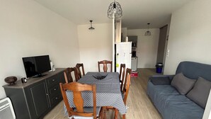 Un espacio habitable compacto con comedor, sofá, televisor y kitchenette.