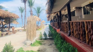 Un complexe hôtelier situé en bord de mer, doté de bâtiments à toits de chaume, de palmiers et offrant une vue dégagée sur l’océan.
