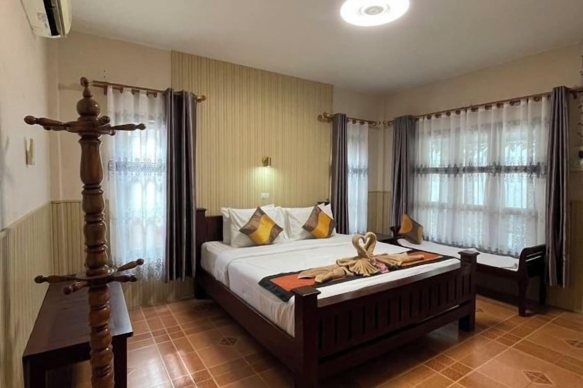 A hotel room with a wooden bed, a bedside table, and a window with curtains.