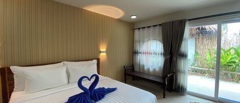 A hotel room with a bed, a bench, a window with curtains, and a view of greenery outside.