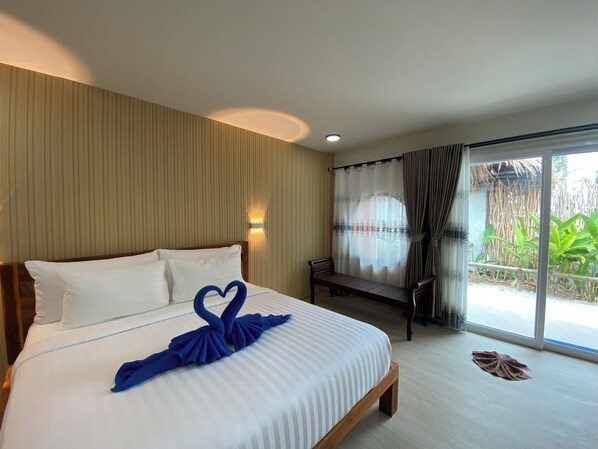 A hotel room with a bed, a bench, a window with curtains, and a view of greenery outside.