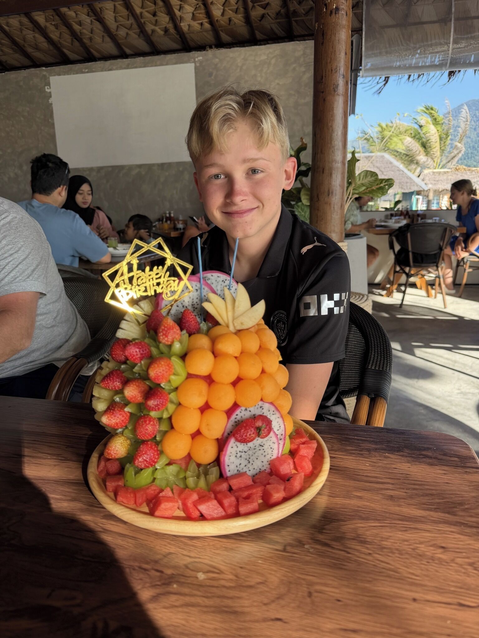 A person seated at a table with a fruit platter in front.