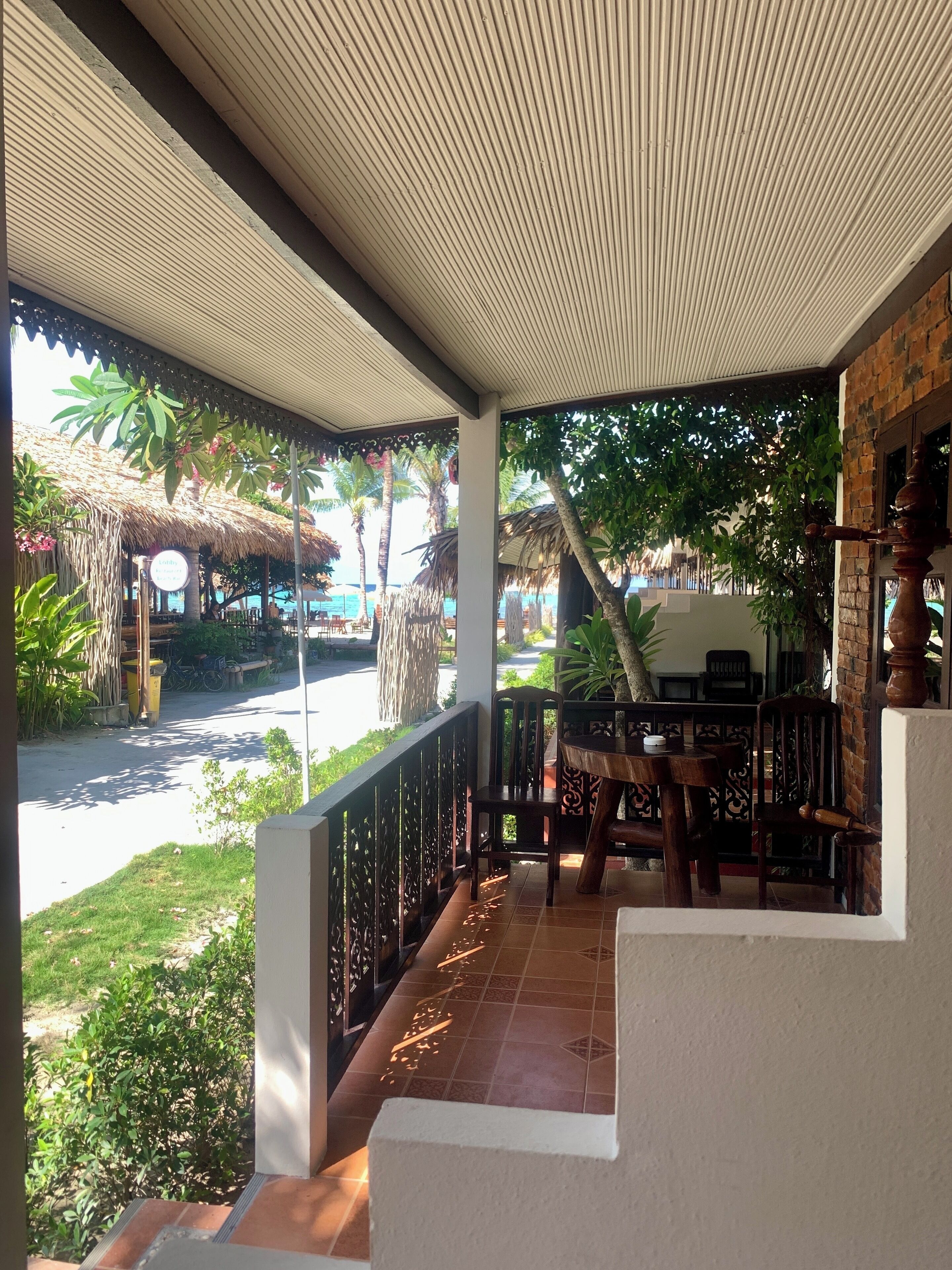 A covered outdoor seating area with a view of a beach and palm trees.